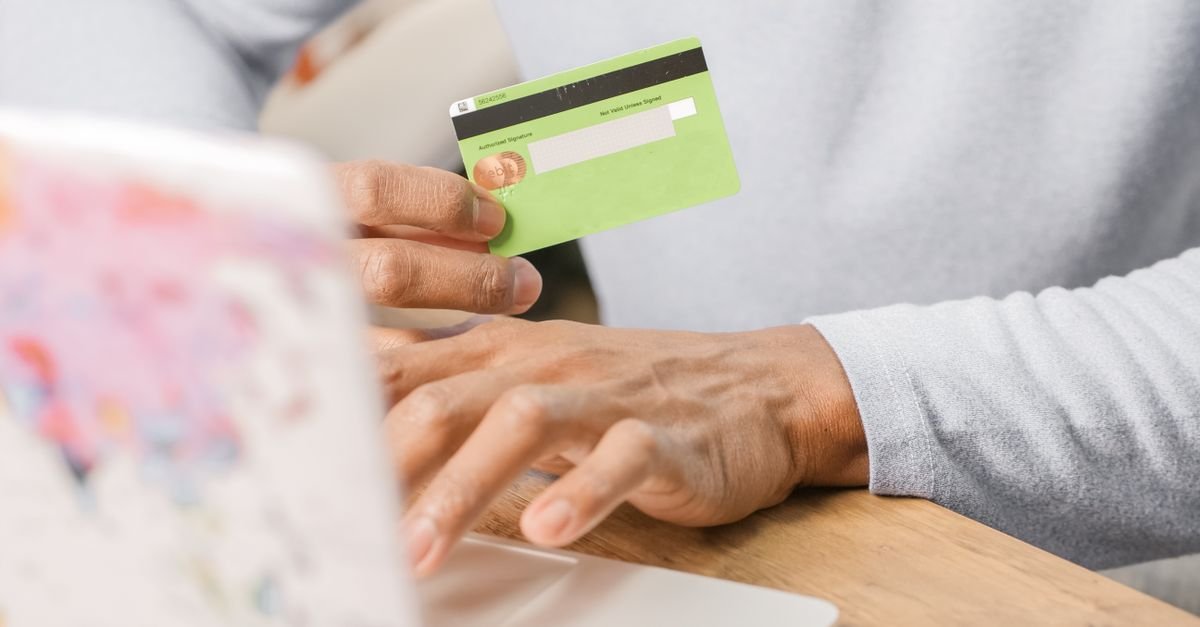 Hands holding a credit card next to a laptop while paying online, representing recurring software subscriptions